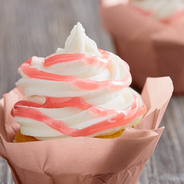 A close up of a cupcake with pink and white Satin Ice glitter glaze swirls.