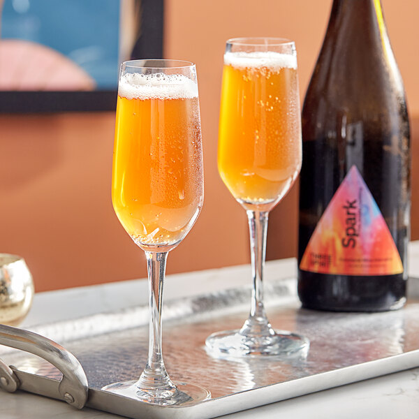 A bottle of Three Spirit Spark Non-Alcoholic Sparkling Rose on a tray with two wine glasses.