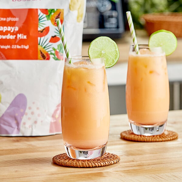 A glass of Bossen papaya orange juice with a straw and lime slice.