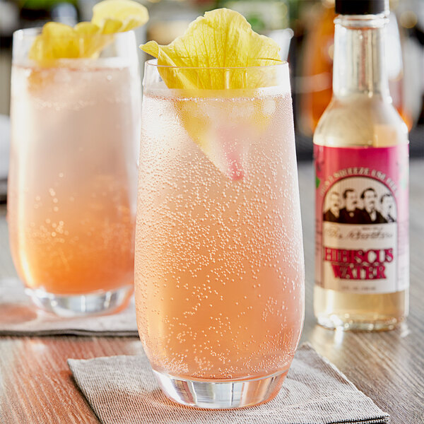 A glass of pink liquid with a hibiscus flower garnish on a table.