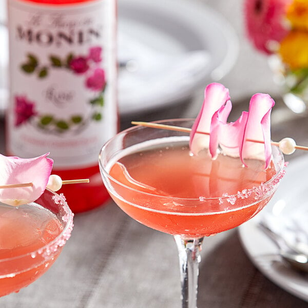 Two glasses of pink drinks with rose petals on them on a table in a cocktail bar.