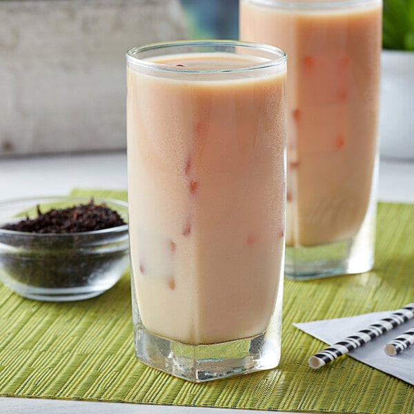 A glass of iced milk tea made with Assam black tea, with another glass and a bowl of loose leaf tea in the background.