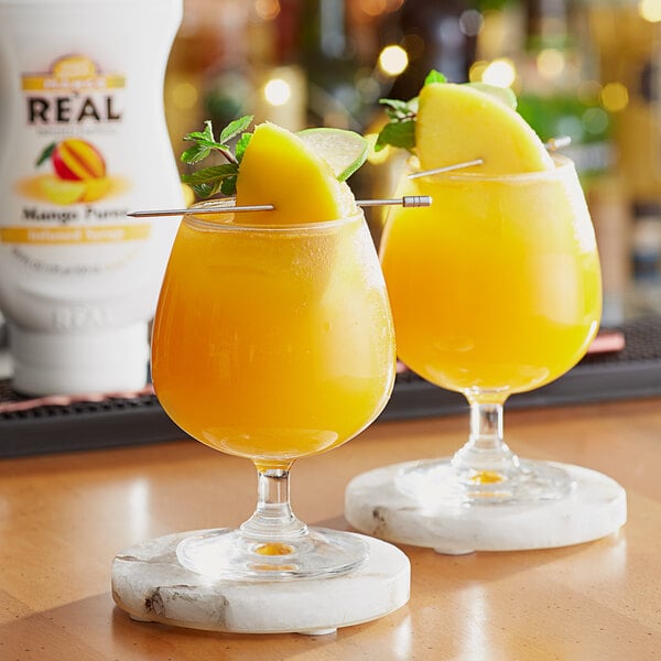 A table in a cocktail bar with two glasses of orange juice with mango puree and lime.