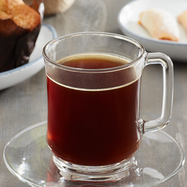 A glass of Ellis 1854 Roast coffee on a saucer next to a brown muffin.