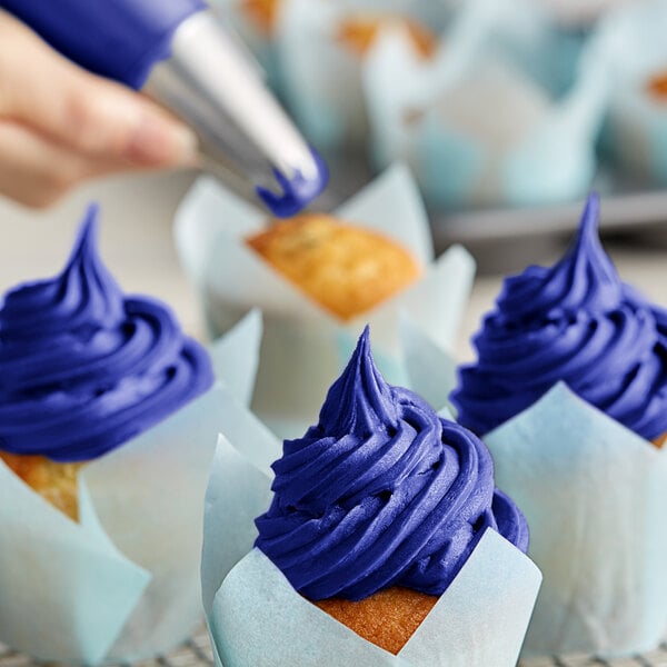 A person using Chefmaster royal blue food coloring to decorate cupcakes with blue icing.