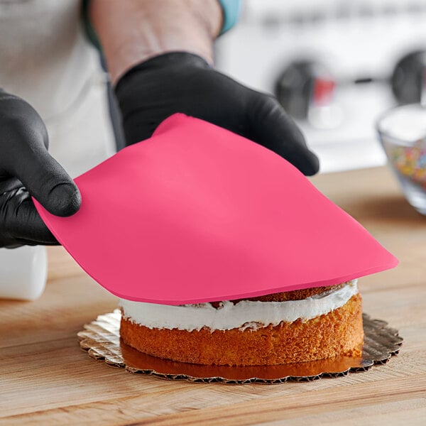 A person wearing black gloves and holding a pink cloth over a cake with Satin Ice pink fondant.