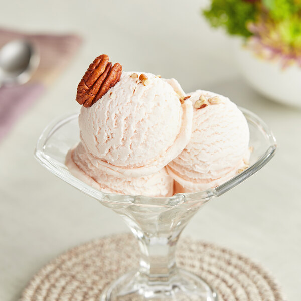 A glass bowl with three scoops of Lloyd's of Pennsylvania Butter Pecan ice cream topped with pecans.