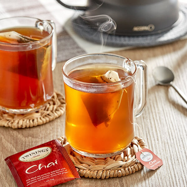 A table with two glass mugs of Twinings Chai Tea and a spoon on it.