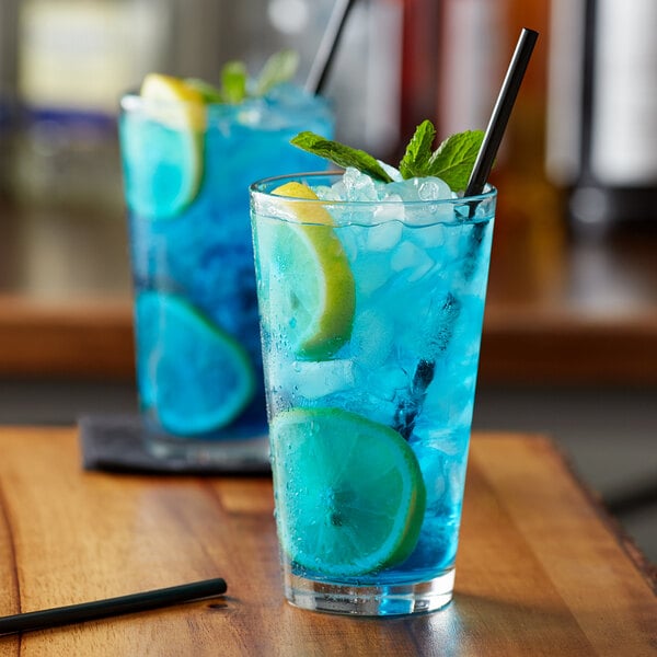 A glass of blue liquid with a lemon slice and mint leaves.
