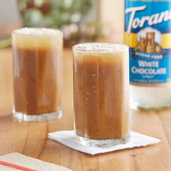 Two glasses of iced coffee with Torani Sugar-Free White Chocolate syrup on a table.