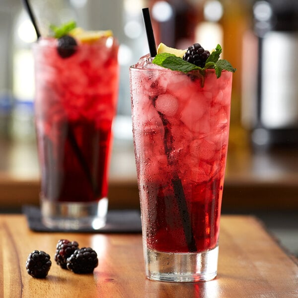 A glass of red liquid with ice and blackberries and mint on the rim.