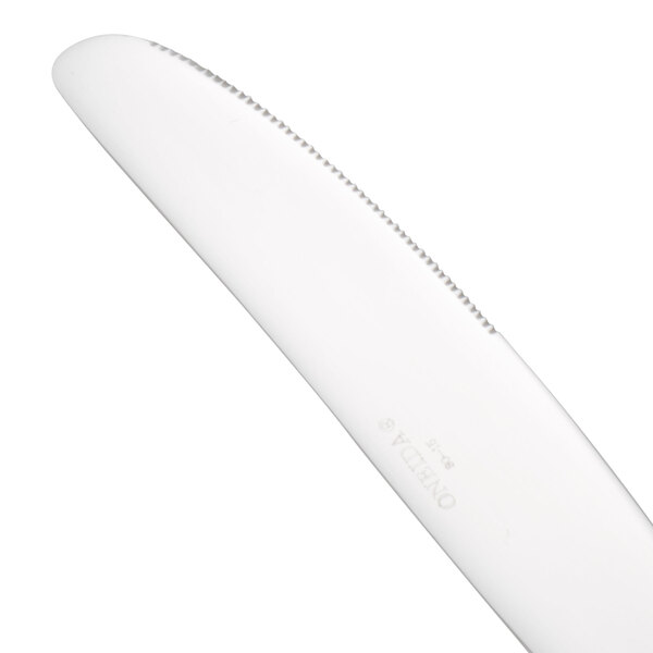 A Oneida Rosewood stainless steel dinner knife with a white handle.