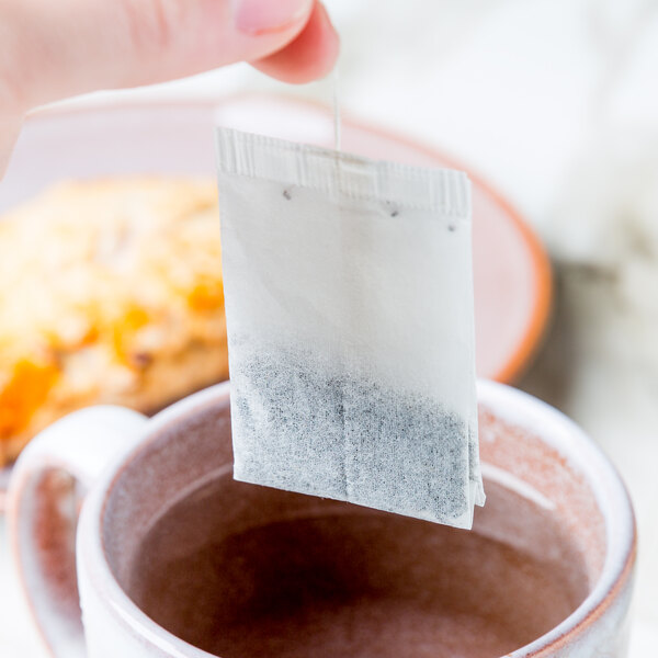 A hand holding a Bromley Organic Black Tea bag over a cup of water.