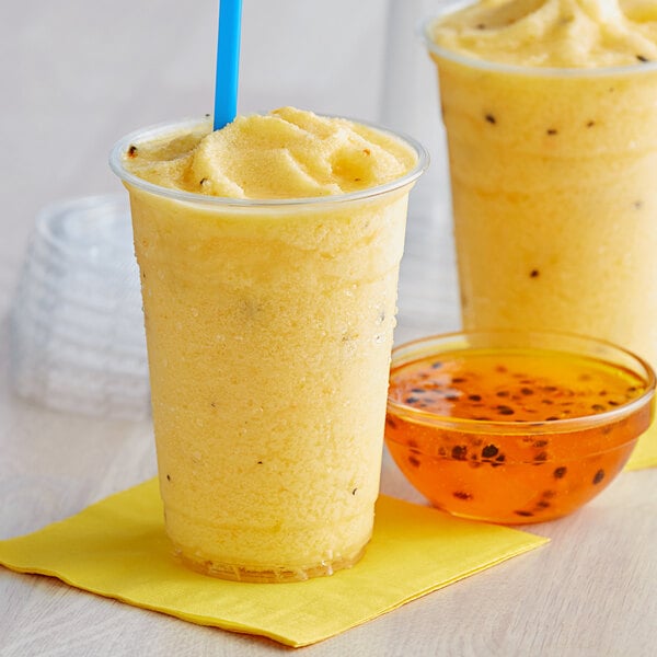 A yellow passion fruit smoothie in a plastic cup with a straw.