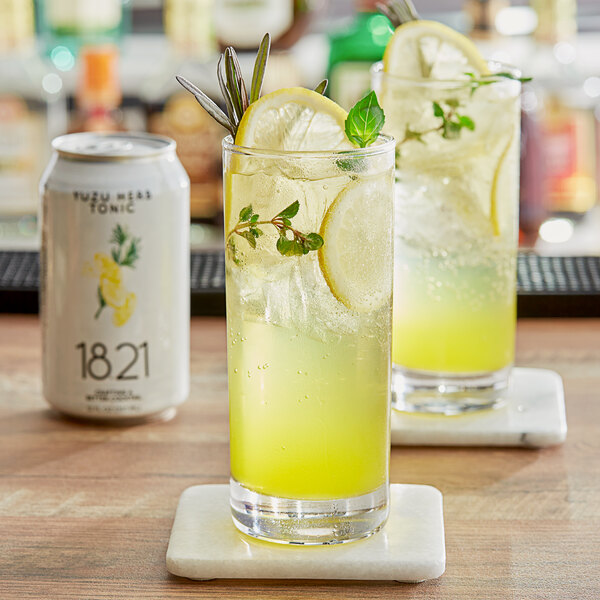Two glasses of yellow Yuzu Herb Tonic with ice and mint on a table.