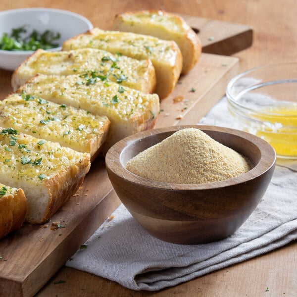 A sliced bread with garlic and herbs on a cutting board with a bowl of Regal Granulated Garlic.