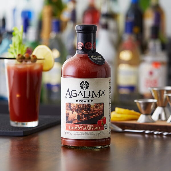 A bottle of Agalima Organic Bloody Mary Mix on a table with a glass of red liquid.