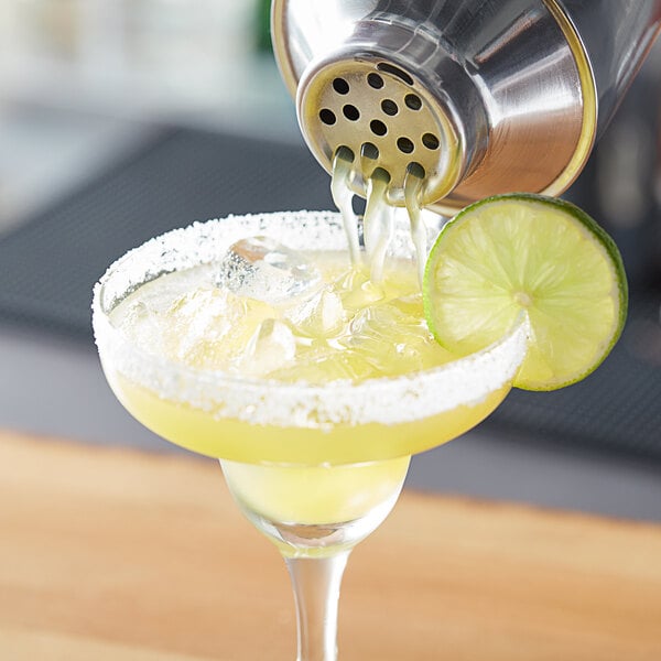 A person pouring Island Oasis margarita into a glass with a lime wedge.