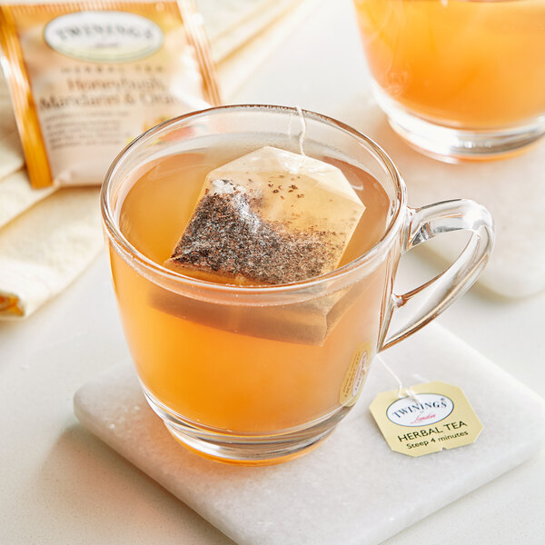 A glass mug with a Twinings Honeybush, Mandarin & Orange tea bag in it on a plate.