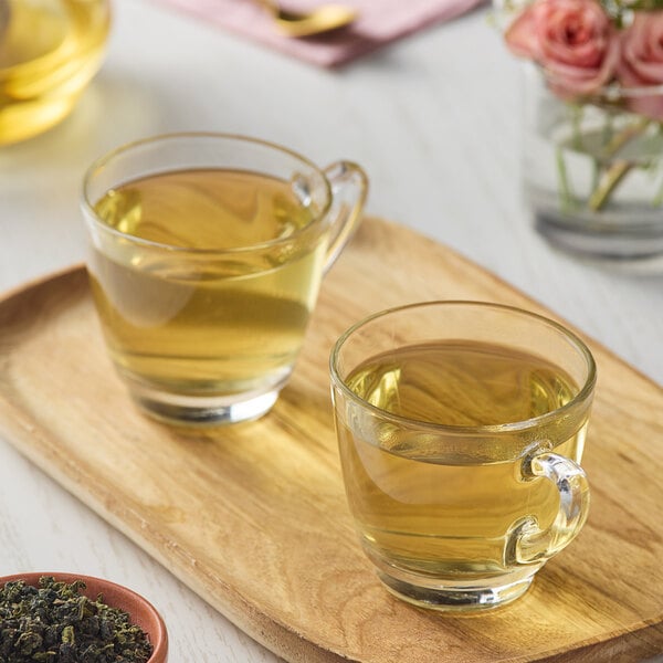 A wooden tray with two glass cups of Numi Organic Ti Kuan Yin-Iron Loose Leaf Tea.