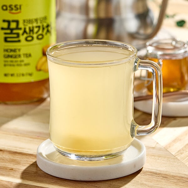 A glass mug with clear liquid and a jar of honey on the side.