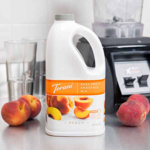 A white plastic bottle of Torani Peach Fruit Smoothie Mix on a counter next to a blender.