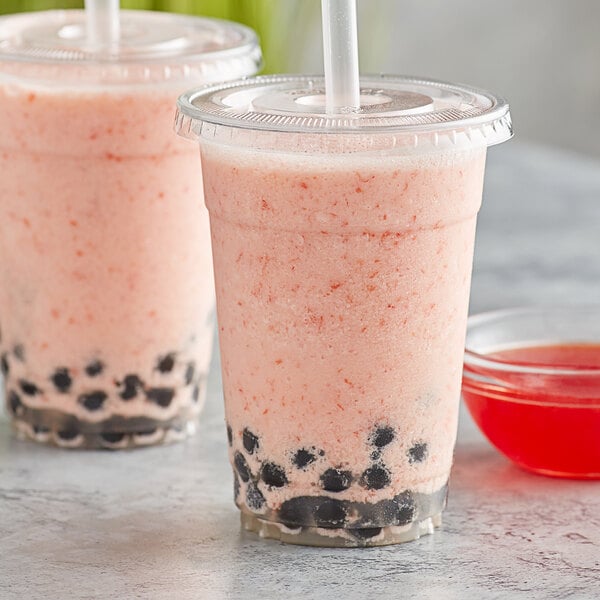 A plastic cup of pink grapefruit smoothie with black balls.