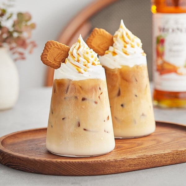 Two glasses of iced coffee with Monin Cookie Butter syrup and cookies on a table.