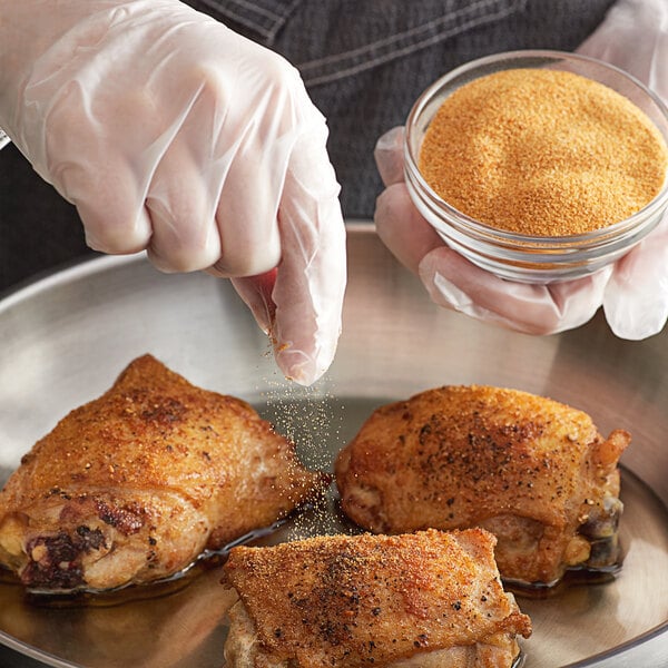 A person sprinkling Regal Roasted Garlic Granules on chicken in a pan.