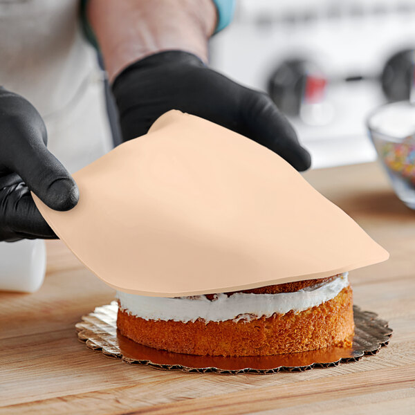 A person wearing black gloves cuts a peach vanilla cake covered in Satin Ice rolled fondant.