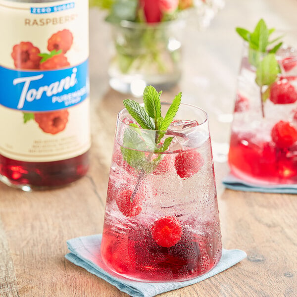 A glass of red raspberry drink with mint leaves.