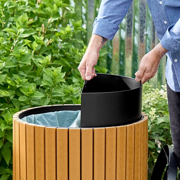 A round outdoor trash can or recycling bin with a wood and stainless steel exterior and a removable black inner compartment.
