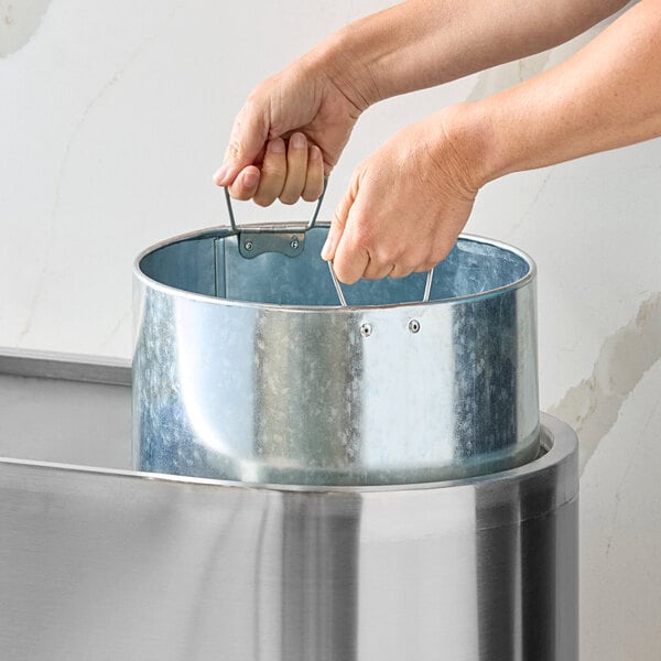 A person lifting a metal liner from a stainless steel decorative indoor three-stream trash can.