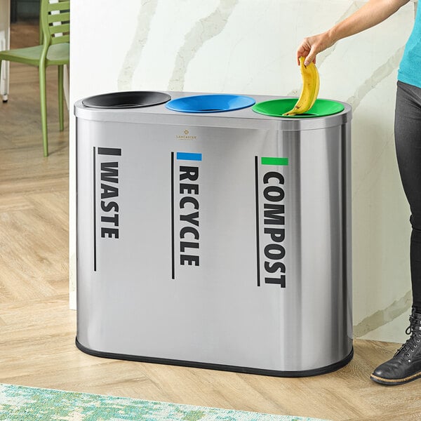 A stainless steel indoor trash can with three separate labeled compartments for waste, recycling, and compost.