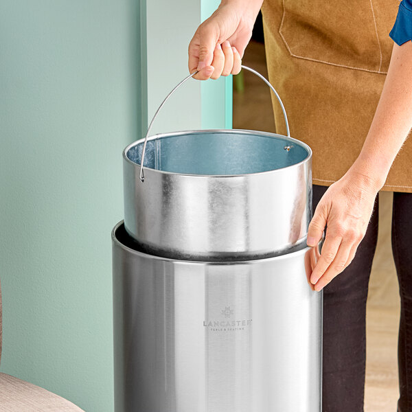 A stainless steel round decorative trash can with a removable inner bucket and swivel lid.