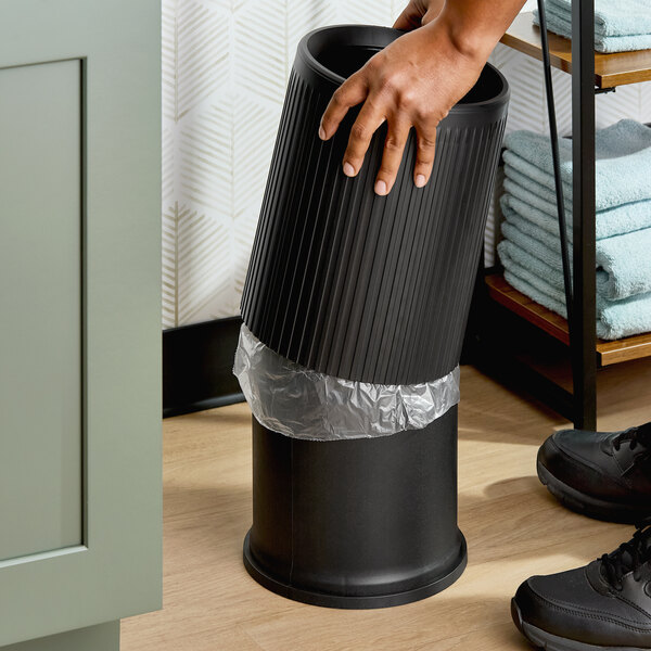 A black round polyethylene decorative wastebasket with a removable lid and a trash liner inside.