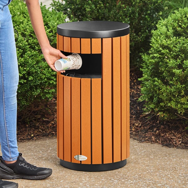 A round outdoor trash can with a wood composite exterior and a side opening.