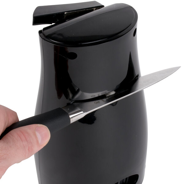 A person using a Proctor Silex black electric can opener to sharpen a knife.