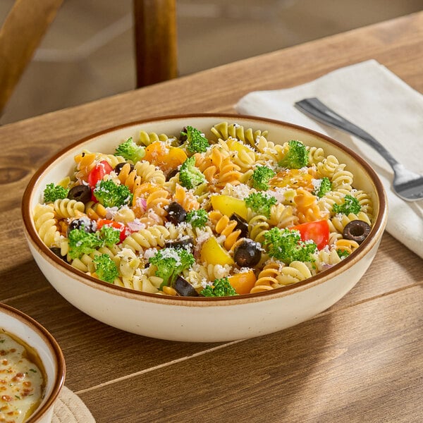 A porcelain coupe low bowl filled with pasta salad and vegetables.