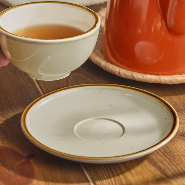 A hand holding a cup of tea on a Granite Gray Acopa Keystone porcelain saucer.
