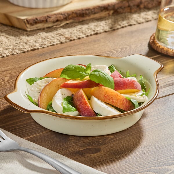 A round, shallow vanilla bean porcelain casserole dish filled with a fresh salad, placed on a wooden table.