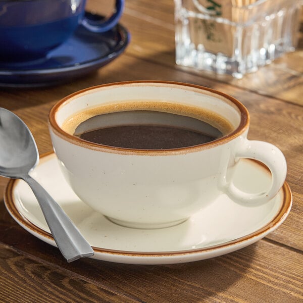 An Acopa Keystone porcelain cup of coffee on a saucer with a spoon.