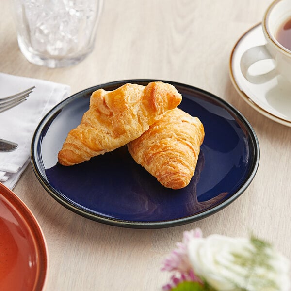 An Acopa Keystone Azora Blue porcelain coupe plate with a plate of croissants and a cup of tea on a table.