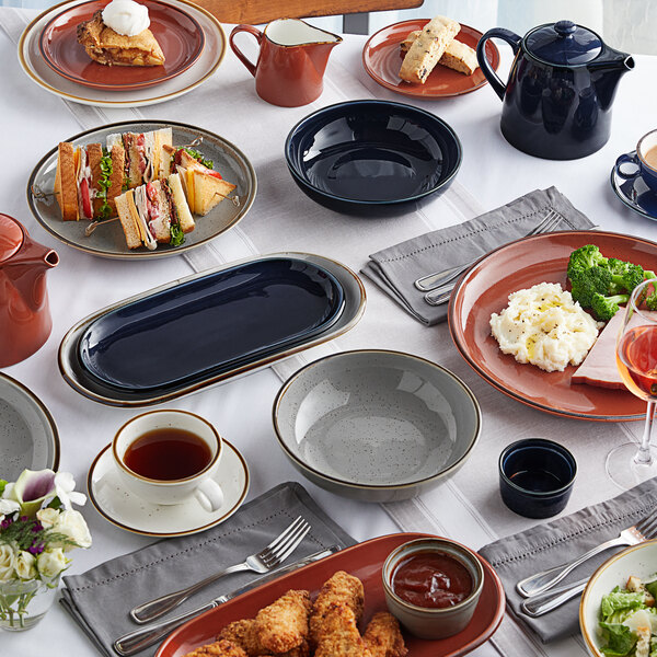 An Acopa Keystone white porcelain mini casserole dish with a lid on a table with plates of food.