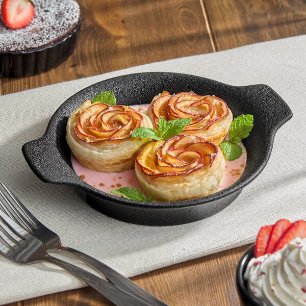 A Acopa Keystone porcelain shirred egg casserole dish with food in it, next to a fork and knife.