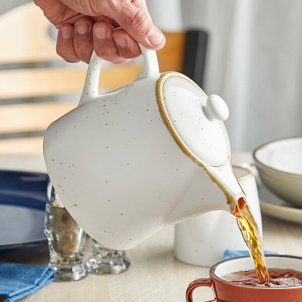 A hand pouring tea into an Acopa vanilla bean porcelain teapot.
