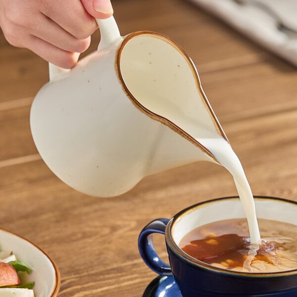 A white porcelain creamer pitcher pouring milk into a cup of coffee.