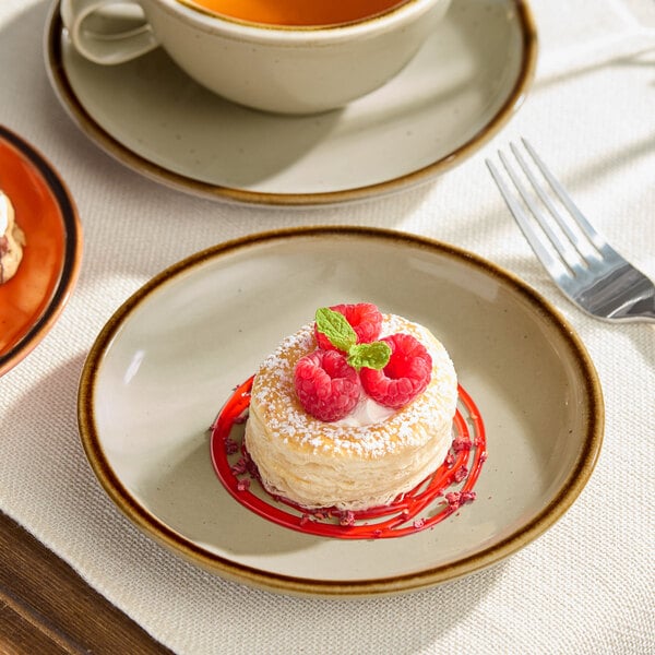 An Acopa Keystone granite gray porcelain coupe plate with a dessert and raspberries on a table.