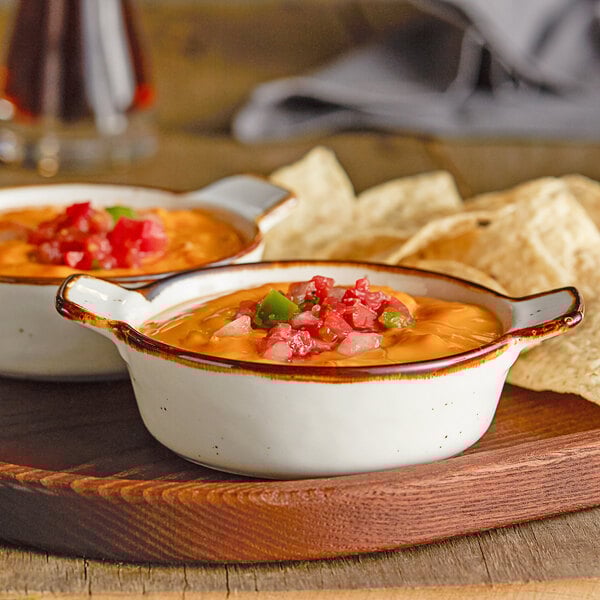 Two Acopa Keystone porcelain mini casserole dishes filled with food next to tortilla chips on a wooden tray.