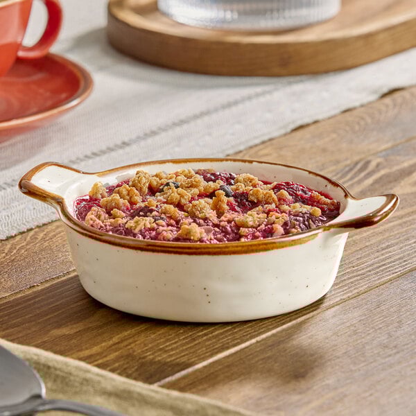 A small vanilla bean porcelain mini casserole dish with handles, filled with a berry crumble dessert.